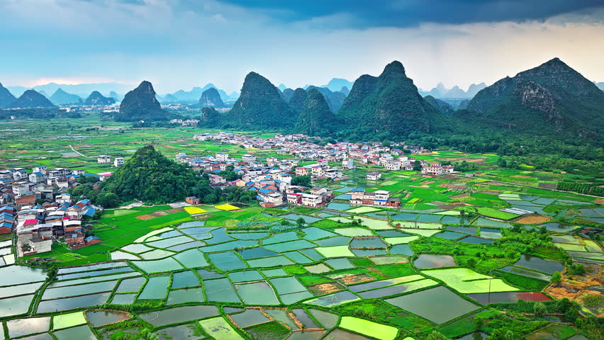 Aerial shot of the beautiful rural landscape with green paddy fields, villages, and spectacular karst mountain scenery in Guilin, China.