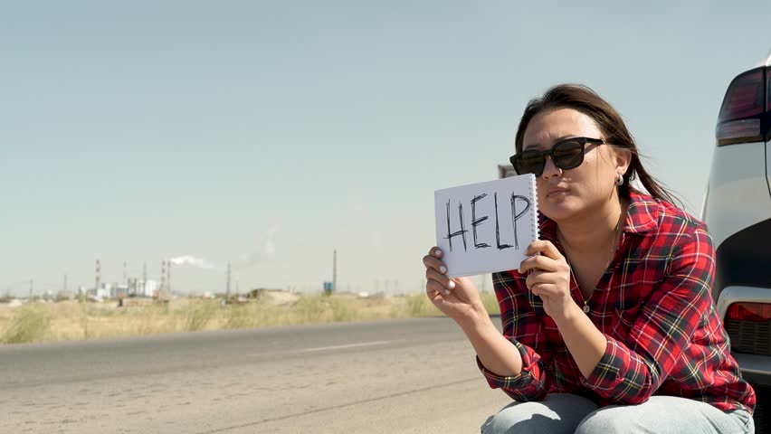A woman is sitting on the side of a road, holding a sign that says HELP