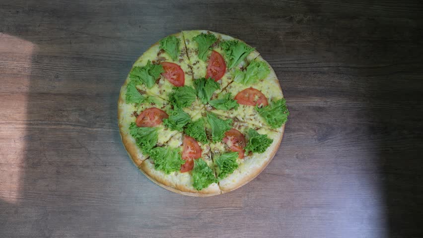 Close-up of a freshly baked pizza with lettuce leaves on a wooden plate. Delicious freshly baked pizza with sausage, cheese and herbs in the pizzeria. The concept of catering. Stabilized camera image.