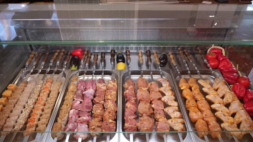 Close-up of various types of kebabs and meat snacks on skewers before cooking. The process of preparing meat for barbecue in the restaurant kitchen. The concept of catering and takeaway food.