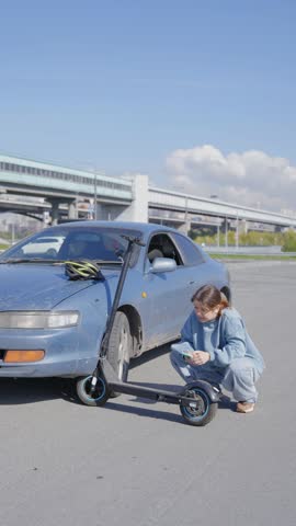 Woman examines and photographs the damage caused by a collision between an electric scooter and a car.