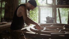 Woodworker in hat applies lacquer onto round wooden frame in workshop. Skilled mature craftsman maintains damage of vintage door working in carpentry shop - Powered by Shutterstock - Get 15% off with code: PIKWIZARD15