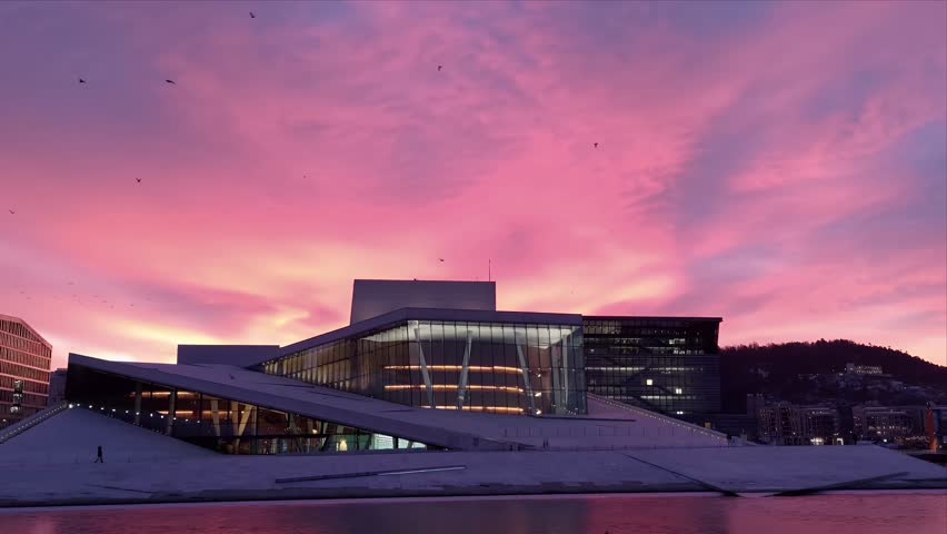 Stunning view of the Oslo Opera House at dawn, with a pink and purple sunrise sky reflecting on the calm harbour waters in Oslo, Norway.