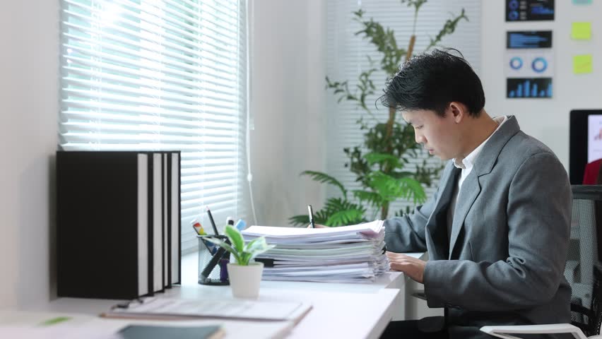 Asian businessman reviewing documents at desk.