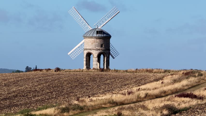 Moving from low to high: A windmill in the English countryside during summer in daylight. Aerial drone footage with superzoom compression in the background. Chesterton mill