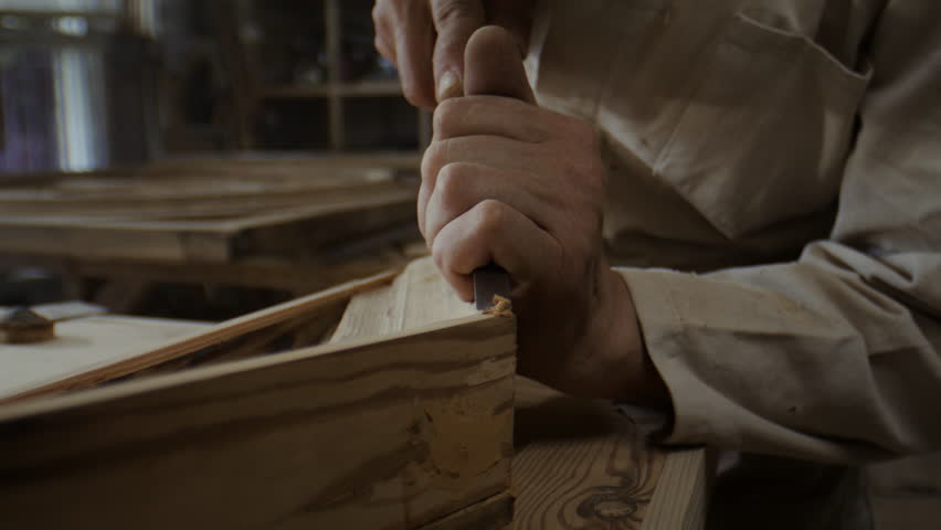 Skilled man weathered hands correct wooden door frame corner with sharp chisel slow motion. Craftsman adjusts fragile angle carefully creating smooth clean edge