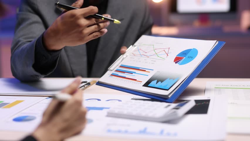 Business people analyzing financial charts and graphs, discussing company growth and planning investment strategies in a collaborative office.