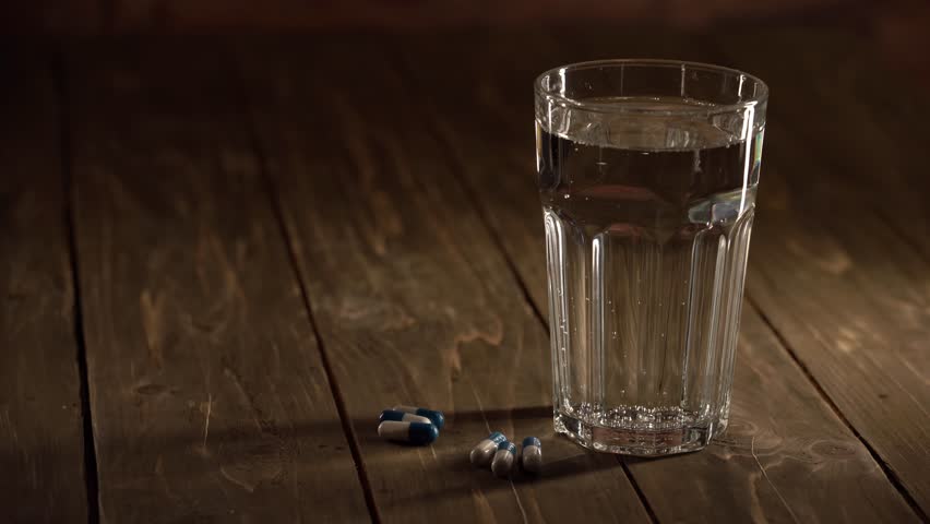 The capsules next to a glass of water on a wooden table, close-up. A daily dose of medicine to maintain health.