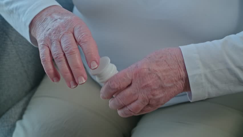 Senior woman with tremor trying to take pills out from a bottle, medical support with prescription and painkillers