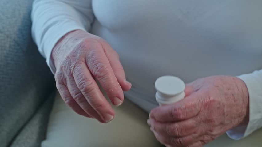 Unrecognizable senior woman and her son, helping take pills out from a bottle, Parkinson's disease. 