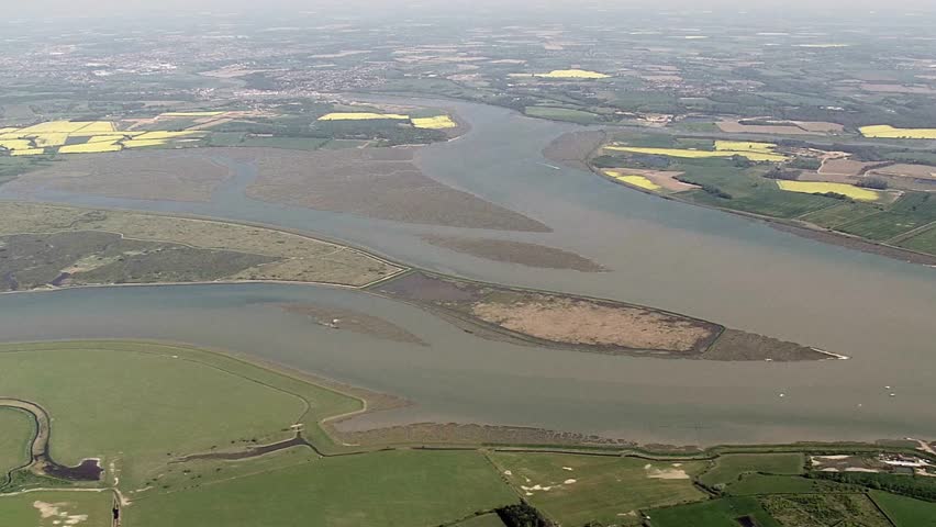Aerial view of a wide river flowing through green fields and yellow rapeseed crops