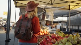 Stylish young woman with leather backpack and hat browsing colorful fruit stall at sunny outdoor farmers market, selecting fresh, organic produce for healthy lifestyle - Powered by Shutterstock - Get 15% off with code: PIKWIZARD15