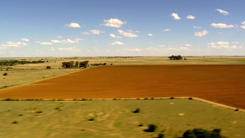 Aerial view of vast farmland with red soil under a blue sky with scattered clouds