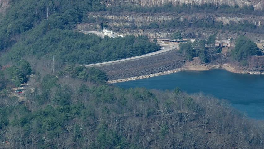 Aerial view of a dam nestled among trees and mountains on a sunny day outdoors