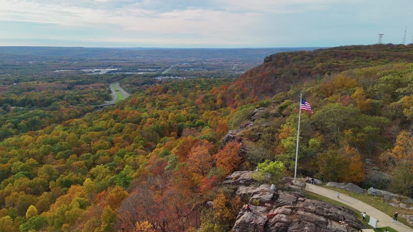 Aerial view of a waving American flag overlooking colorful autumn forest and rolling hills, scenic countryside under cloudy sky. hiking up towards Castle Craig viewpoint, East Peak.
