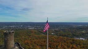 Drone view of a historic stone tower and American flag above a vibrant autumn forest, with scenic hills and blue sky in the background. Castle Craig viewpoint. East Peak - Powered by Shutterstock - Get 15% off with code: PIKWIZARD15