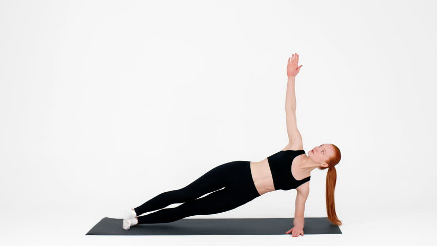 Young woman practicing side plank exercise for fitness in a bright studio