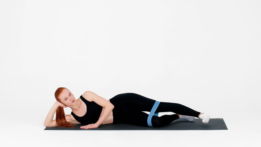 Young woman practices pilates with resistance band on mat in bright studio