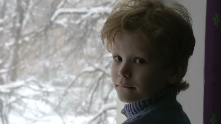 Boy Looks at Snow. Cute redhead boy looks at the camera with wondering eyes. Against the background of the snow blizzard
