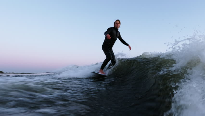 A skilled surfer gracefully rides the wave, showcasing impressive balance and style while navigating the beautiful water under a serene twilight sky.