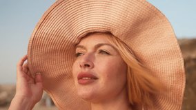 Closeup of young blond woman wearing sunhat enjoying breeze at beach, capturing summer relaxation, holiday and freedom - Powered by Shutterstock - Get 15% off with code: PIKWIZARD15