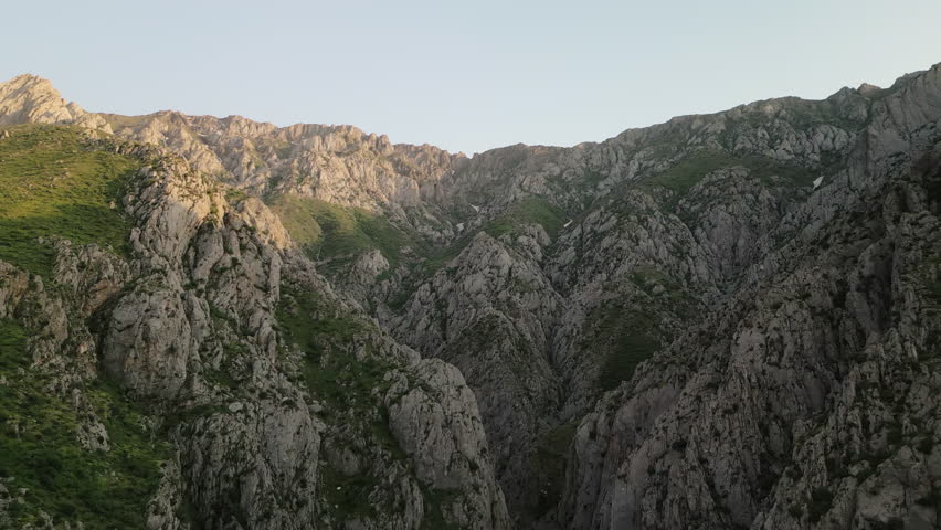 Aerial view of a connected ridge system over a deep canyon in Uzbekistan at dawn. Long lines create motion, cool shadow meets warm sunlight, the landscape promises adventure and serenity