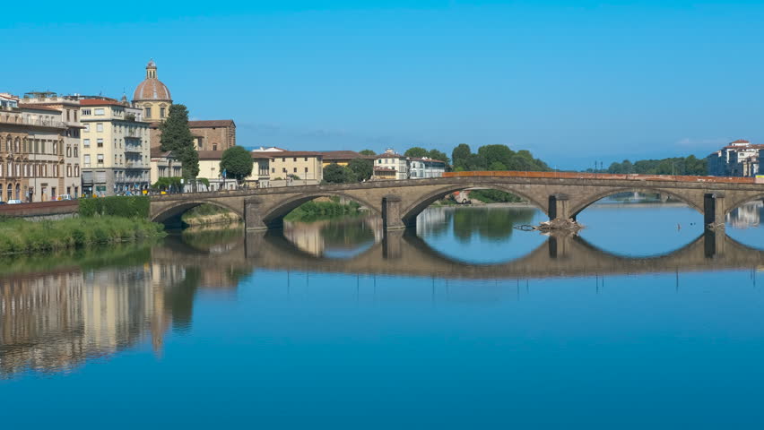 Ponte santa trinita reflecting on arno river in florence. Serene waters of arno river mirroring historic ponte santa trinita and surrounding renaissance architecture under pristine blue sky