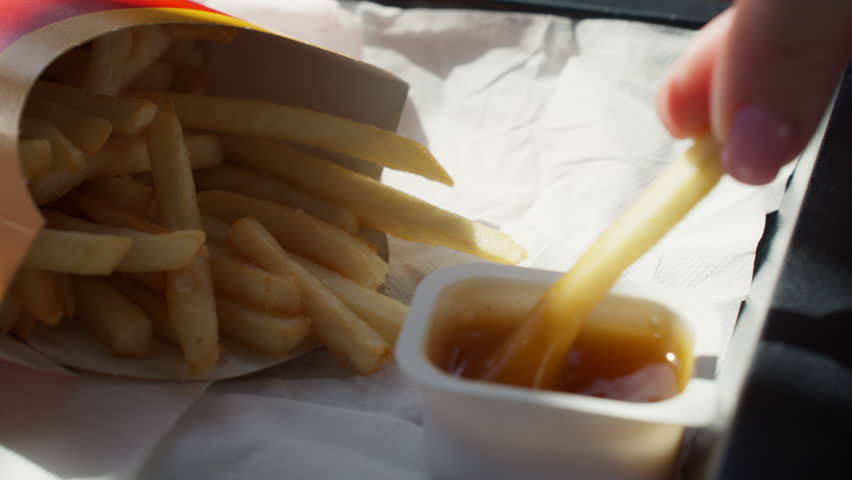 Close-up of hand dipping crispy golden french fry into tangy sweet and sour sauce, classic fast-food snack moment—crispy, saucy, indulgent and irresistible