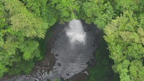 Dense Bali rainforest opens around a circular plunge pool as a powerful waterfall thunders into clear water. Mist rises and ripples move across the basin in bright daytime light. Tropical travel scene - Powered by Shutterstock - Get 15% off with code: PIKWIZARD15