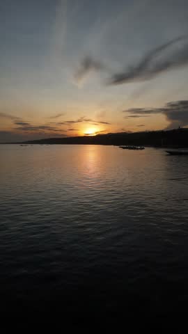 Aerial drone view of a calm ocean at sunrise with small fishing boats on the water. Golden morning light reflecting on gentle waves. Peaceful tropical seascape from above.