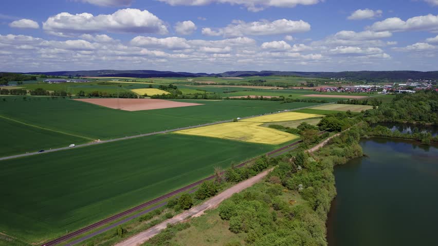 Aerial view of lush green and yellow agricultural fields under a blue sky with clouds.