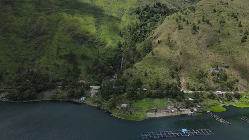 Cinematic aerial drone footage revealing the breathtaking beauty of Lake Toba from Bakkara Valley, Baktiraja. The shot captures the magnificent volcanic lake surrounded by majestic green cliffs, lush agricultural fields, and local settlements in Humbang Hasundutan. This footage highlights a perfect blend of natural landscape, cultural heritage, and the peaceful atmosphere of one of the world