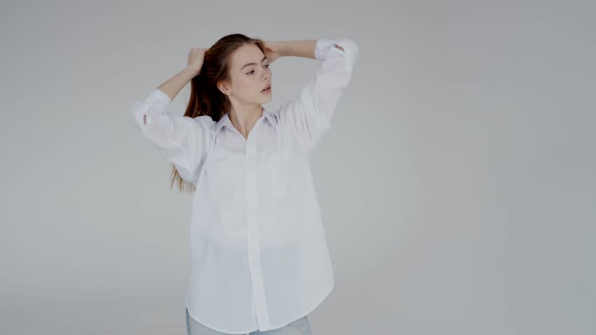 Portrait of a young woman with long hair, smiling gently, dressed in a casual white shirt and jeans on a grey background. Young Woman Smiling in Casual White Shirt and Jeans
