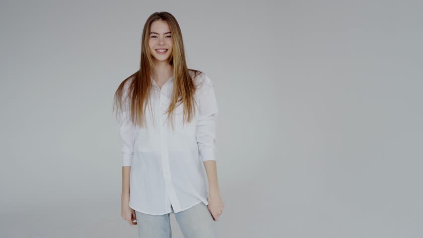 Portrait of a young woman with long hair, smiling gently, dressed in a casual white shirt and jeans on a grey background. Young Woman Smiling in Casual White Shirt and Jeans