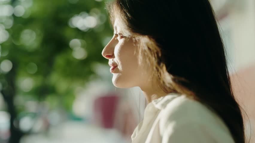 Close-up portrait of a woman with long hair, smiling warmly in a natural outdoor setting with soft sunlight filtering through trees in the background. Close-Up Portrait Of A Woman With Long Hair