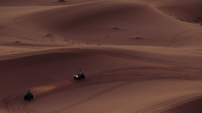People riding quad bikes over the sand dunes in Morocco at sunset. This exciting activity is a popular tourist attraction and a great way to experience the desert landscape.