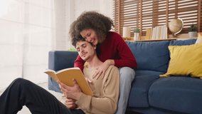Latina young couple sitting together on sofa in living room at home. Attractive man and woman feel happy and relax, enjoy spending leisure quality time reading book on holiday vacation in cozy house. - Powered by Shutterstock - Get 15% off with code: PIKWIZARD15