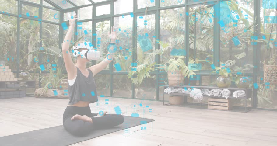 Woman with VR headset raising arms activating blue icons settling into meditation pose in sunroom. Digital, mindfulness, wellness, serenity, futuristic, nature, relaxation