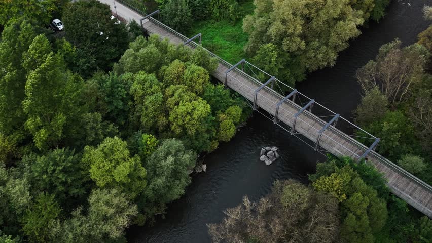 Aerial view of a wooden bridge over a river surrounded by autumn trees.