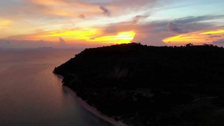 Tropical island silhouette at sunset with vibrant colors reflecting on the ocean