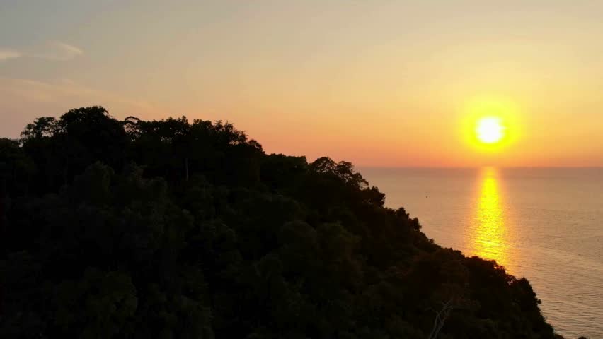 Tropical island hill with dark green trees at sunset overlooking the golden ocean