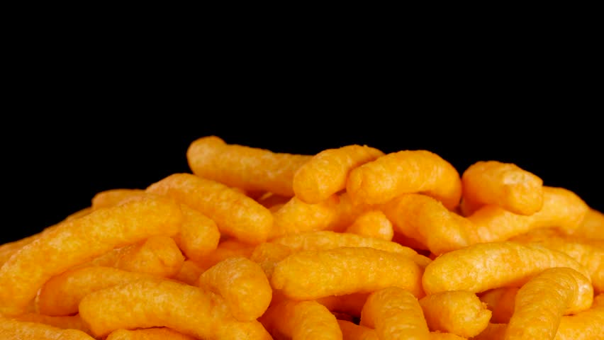 Human hand picks crispy cheese puffs under studio lighting, close-up, black background, smooth camera