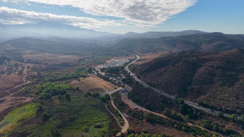 Aerial view of a winding highway cutting through rugged canyon terrain under a dramatic sky.