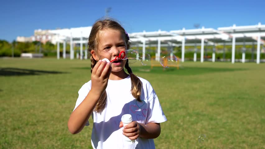 Adorable little girl with pigtails having fun while blowing soap bubbles in a sunny park, enjoying a beautiful day outdoors with her family and creating magical moments during childhood