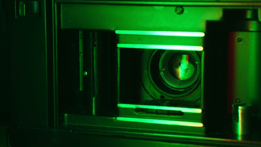 Mechanical shutter of an old analog camera opening and closing in a dark environment with green lighting, showing the lens aperture and internal components working in a close up view