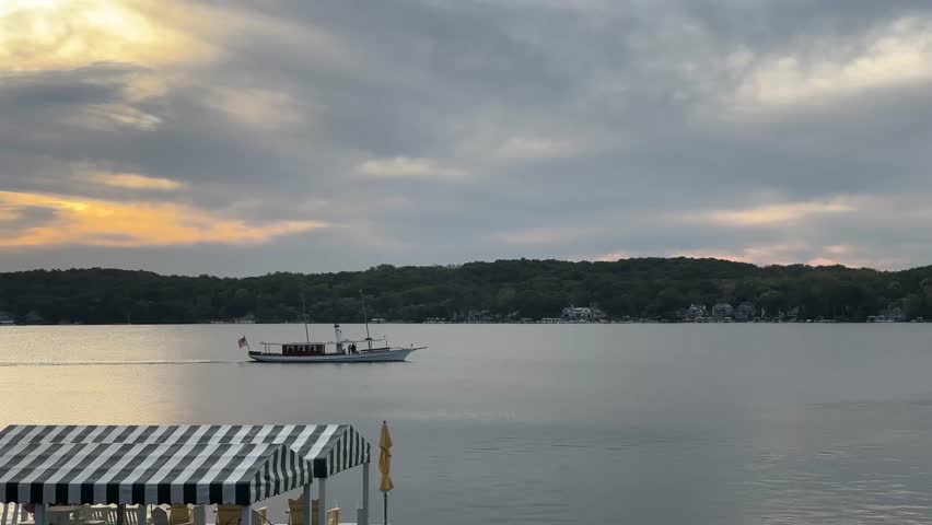 Boat Cruising Across Calm Lake Geneva In Wisconsin, USA Under Cloudy Sunset Sky. wide shot