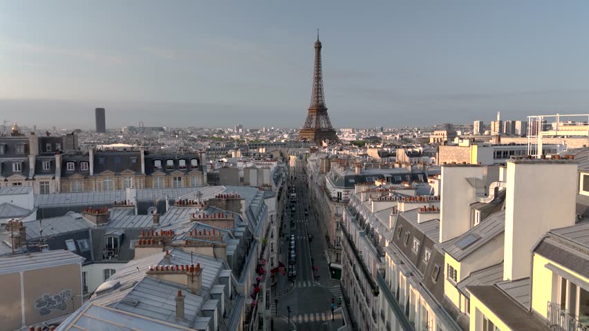 Aerial drone view of the sleepy streets of Paris, France, overlooking the famous Eiffel Tower and Champ de Mars at sunrise or sunset. Low motion over the rooftops. Cinematic 4k. Europe from above.