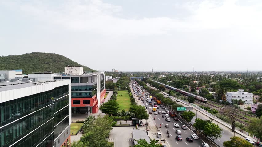Growth in a Metro City: Aerial view contrasting a modern, glass-faced corporate building and manicured lawns with the dense, chaotic traffic and a train passing through a bustling urban landscape