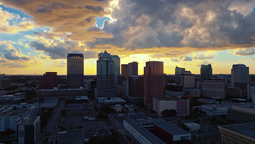 Aerial orbital view of the Tampa skyline after sunset has set in with dramatic clouds glowing in the sky and warm light reflecting on buildings.