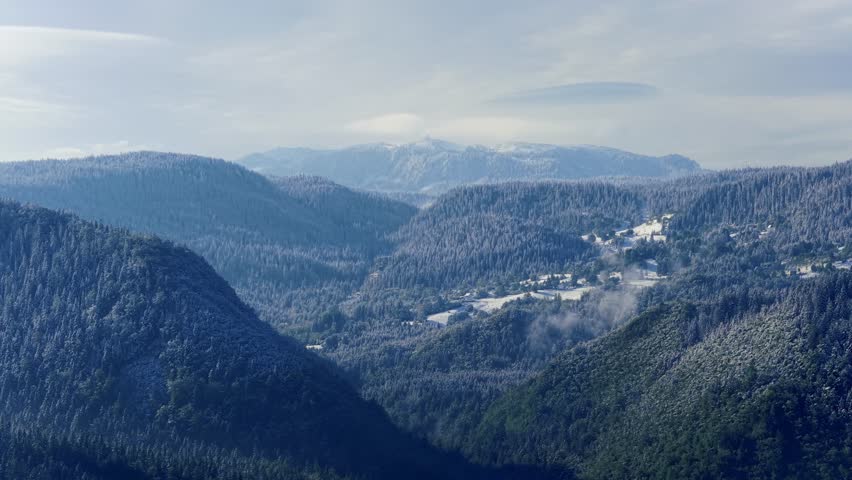 Peaceful view of wooded mountain slopes and open valley filled with gentle daylight and distant haze